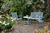 Seating area with metal furniture in a green courtyard in front of an overgrown wall