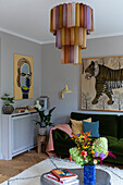 Living room with colourful hanging lamp above coffee table and dark green velvet sofa