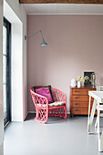 Pink rattan chair with cushion next to wooden chest of drawers in the dining room