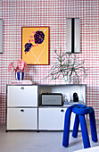 Living room with white shelf, blue designer stool and colourful mural in front of chequered wallpaper