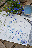 Watercolour drawings of blue flowers and grasses on a wooden table