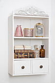 White wall shelf with glass bottles, old books, candles and decorative picture frame
