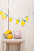 DIY paper lemon garland over wooden stool with pink jug and bowl of lemons