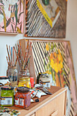 Acrylic colours, brushes and paintings on a wooden cabinet in a studio