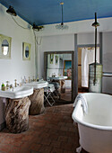 Bathroom with two washbasins on tree-trunk pedestals and free-standing bathtub