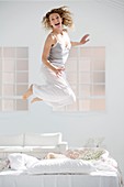 Attractive young woman jumping on her bed