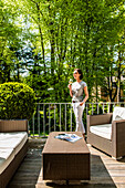 Frau mit Weinglas steht auf einem Balkon mit Loungemöbeln, Hamburg, Deutschland