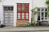  Old front door and lattice window, in front of it a bench and a bicycle 