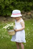 A little girl holding a straw hat filled with daisies