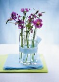 Violette Blumen in kleinen Fläschchen als Tischdeko