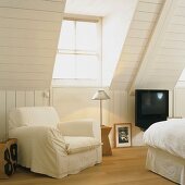 White armchairs next to dormer window in attic bedroom with white wood panelling