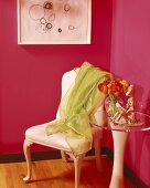 Magentafarbene Zimmerecke mit lindgrünem Tuch auf einem Stuhl und Beistelltisch mit klarer Acrylplatte