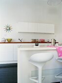 weiße Designer Küche mit Barhockern an der Theke und Strahlen-Uhr an der Wand