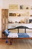 Antique bench with cane backrest and seat cushions in front of floating shelves and vintage wooden cabinet