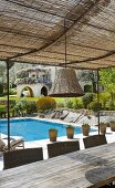 Terrasse mit luftigem Sonnenschutz, Korblampe, Esstisch und mit Swimming Pool im Hintergrund