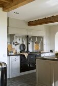 Freundliche Landhausküche mit rustikalen Deckenbalken und antikem, schwarzen Herd zwischen weissen Küchenschränken