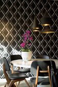 Dining table and chairs in front of sober, geometric wallpaper with purple orchid lightening the atmosphere