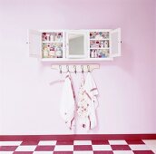 Wandschränkchen mit Badeutensilien über Kleiderhaken an rosafarbene Wand