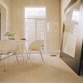 Ein Esszimmer mit weißen Schalenstühlen, eine Stehlampe und ein an der Wand angelehnter Spiegel