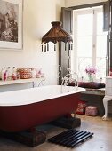 Freistehende rote Badewanne auf zwei Holzbalken unter Hängelampe
