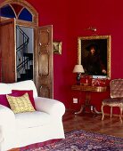 Weisser Sessel in rotem Wohnzimmer mit offener Flügeltür zum Treppenhaus