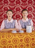 Twins sitting at table in front of bright wallpaper