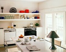 Einfache, freundliche Küche mit langem Geschirregal und weißem Tisch mit Tischlampe