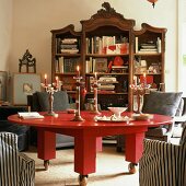Runder, massiver Tisch in Rot mit Rollen vor antikem Bücherschrank mit vielen Büchern