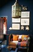 Die antike Sitzbank mit bunten Kissen und viele Metallbilderrahmen bilden einen schönen Blickfang vor der dunkelblauen Wand