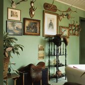 Eine Sammlung von Geweihen und Gemälden in barocken Goldrahmen an einer grünen Wohnzimmerwand