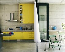 Eine knallgelbe Küchenzeile in einer Küche mit Betonwänden - durch eine Klapptür von der Terrasse getrennt