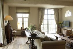 Antike Holzmöbel und ein Polstersofa in einem rustikalen Wohnraum mit großem Rundbogenfenster und Holzbalkendecke