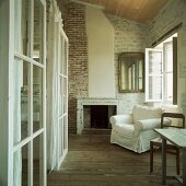 Weisser, schlichter Polstersessel in einem historischen Wohnraum mit Dielenboden und Steinwänden