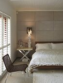 Netzartige Tagesdecke auf dem Bett und moderner Beistelltisch mit Chromklappfüßen vor gepolstertem Wandpaneel
