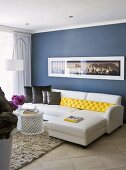 Verschiedenfarbige Kissen auf einem weissen Ledersofa mit Récamière im Wohnzimmer mit blauer Wand