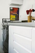 Ausschnitt einer minimalistischen Küchenzeile mit Edelstahloberfläche und weissen Schränken