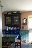 Antikes, blaues Küchenbuffet und bunt bemalter Bauerntisch im Esszimmer mit Steinboden und Wandvertäfelung