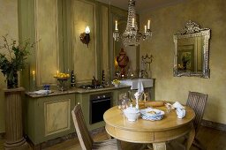 Küche in Grün mit passender Holzvertäfelung, rundem Tisch, Kronleuchter & silbernem Wandspiegel