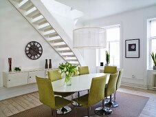 Esszimmer mit ovalem Tisch, grünen Stühlen & Treppenaufgang im Hintergrund