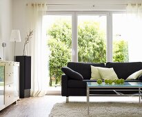 Wohnzimmer mit grauem Sofa & Couchtisch aus Glas vor Terrassentür