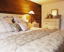 Großes Doppelbett mit gepolstertem Kopfende vor rustikaler Holzwand