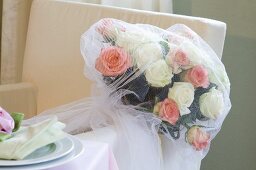 A wedding bouquet of white and pink roses wrapped in a veil