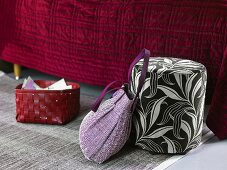 Red basket and bag next to an upholstered stool in front of a bed with a red bedspread