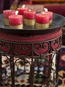 Burning, red candles with gold stripes on a black tray and upholstered stool