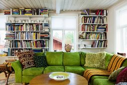 Wohnraum mit grünem Sofa übereck vor Bücherregalen