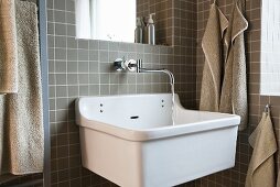 A corner of a bathroom - a sink with a tap mounted on a grey-tiled wall with towels hanging either side