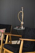 A black 1950s armchair with an occasional table and a water pipe against a black wall