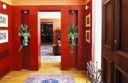 Eleganter Vorraum mit rotverkleideten Wänden und Blumen in Nische mit Blick in Wohnraum