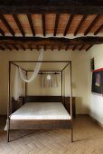 Simple bedroom in a country home with a canopy bed on terracotta flooring and a beam ceiling