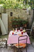 Refreshing drinks on a table with a pink tablecloth and a shelf of flower pots against a high stone wall
